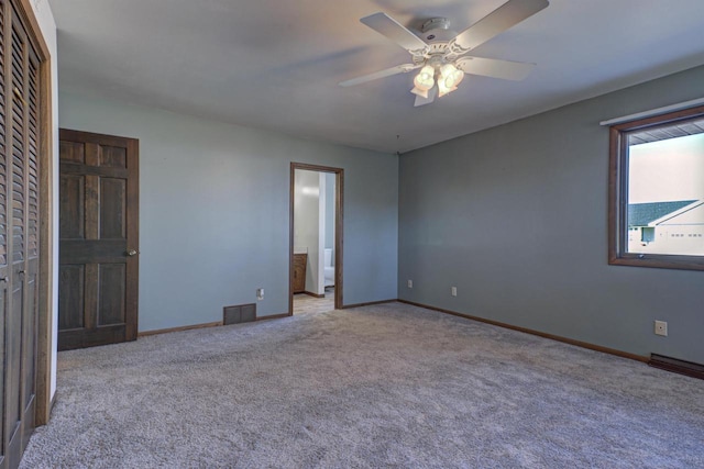 unfurnished bedroom featuring baseboards, visible vents, ensuite bath, ceiling fan, and carpet floors