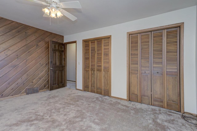 unfurnished bedroom with ceiling fan, carpet floors, wood walls, and multiple closets