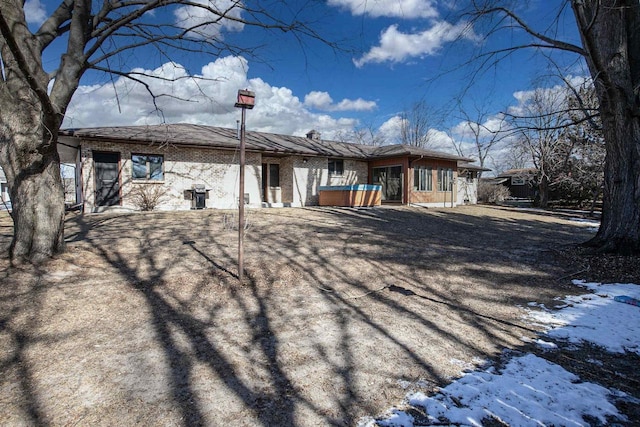 snow covered rear of property featuring brick siding and a jacuzzi