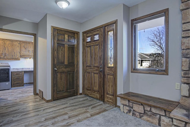 foyer entrance featuring built in desk, washer / clothes dryer, and light wood-style flooring