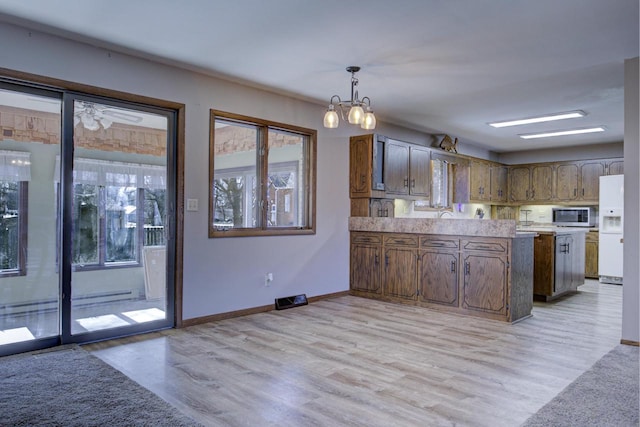 kitchen with a peninsula, baseboards, light countertops, white fridge with ice dispenser, and stainless steel microwave