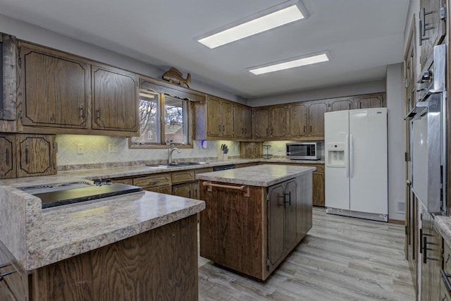 kitchen with white refrigerator with ice dispenser, stainless steel microwave, a sink, light countertops, and backsplash