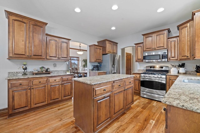 kitchen with stainless steel appliances, arched walkways, a center island, and light wood-type flooring