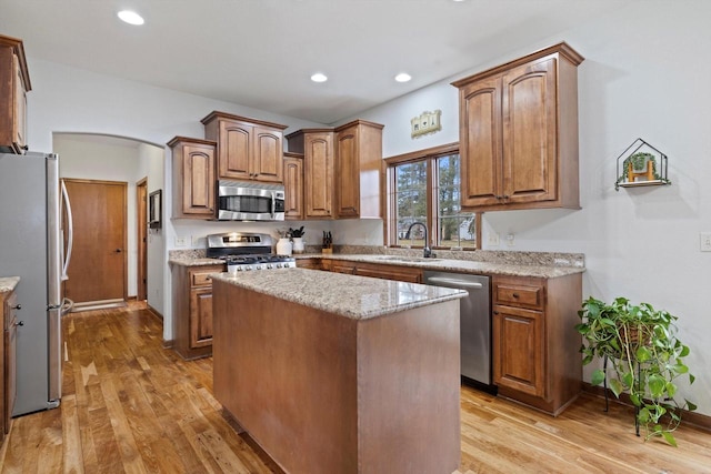 kitchen with arched walkways, stainless steel appliances, a sink, light wood-style floors, and light stone countertops