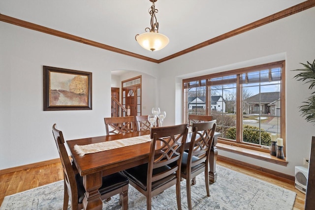 dining space with arched walkways, crown molding, light wood-style flooring, and baseboards