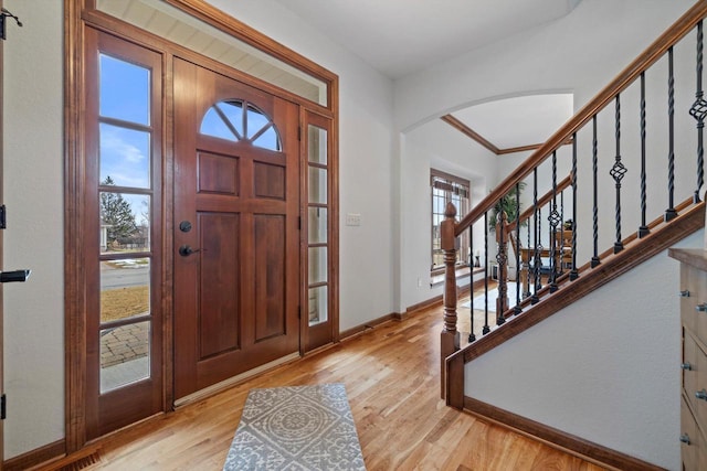 entryway with light wood-type flooring, baseboards, stairs, and arched walkways