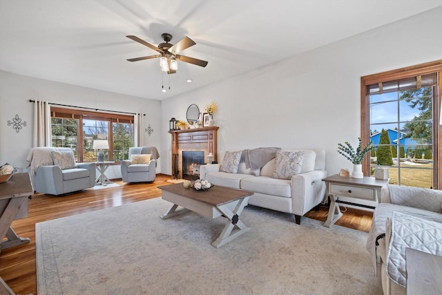 living area featuring a ceiling fan, wood finished floors, and a glass covered fireplace