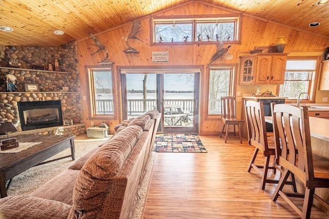 living room with light wood finished floors, wooden walls, wood ceiling, a fireplace, and high vaulted ceiling