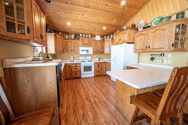 kitchen featuring a breakfast bar, light countertops, wooden ceiling, white appliances, and a peninsula