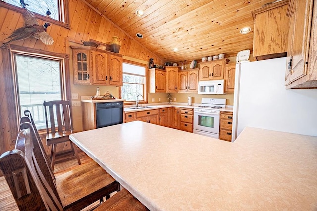 kitchen featuring white appliances, lofted ceiling, a peninsula, light countertops, and a sink