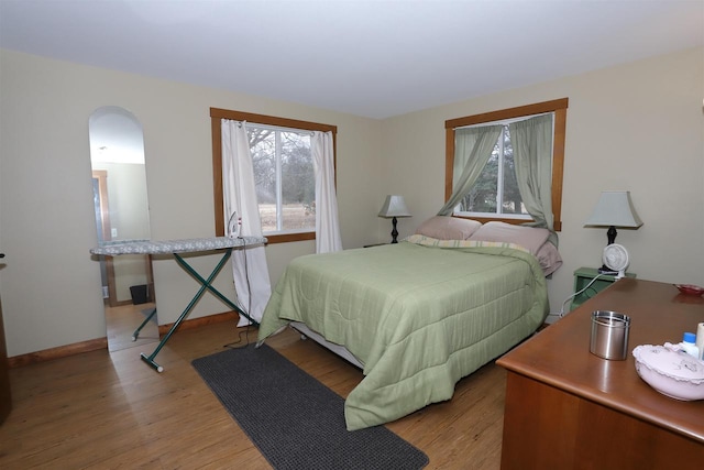 bedroom with arched walkways, baseboards, and wood finished floors