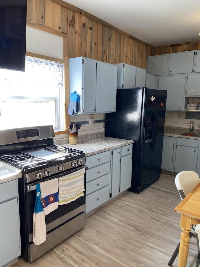 kitchen with light countertops, light wood-type flooring, stainless steel range with gas stovetop, and black fridge