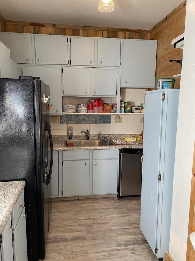 kitchen featuring light wood-style flooring, white cabinets, a sink, dishwasher, and black fridge