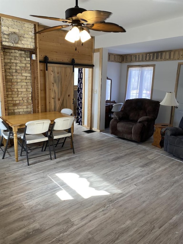 living room with a ceiling fan, a barn door, wooden walls, and wood finished floors