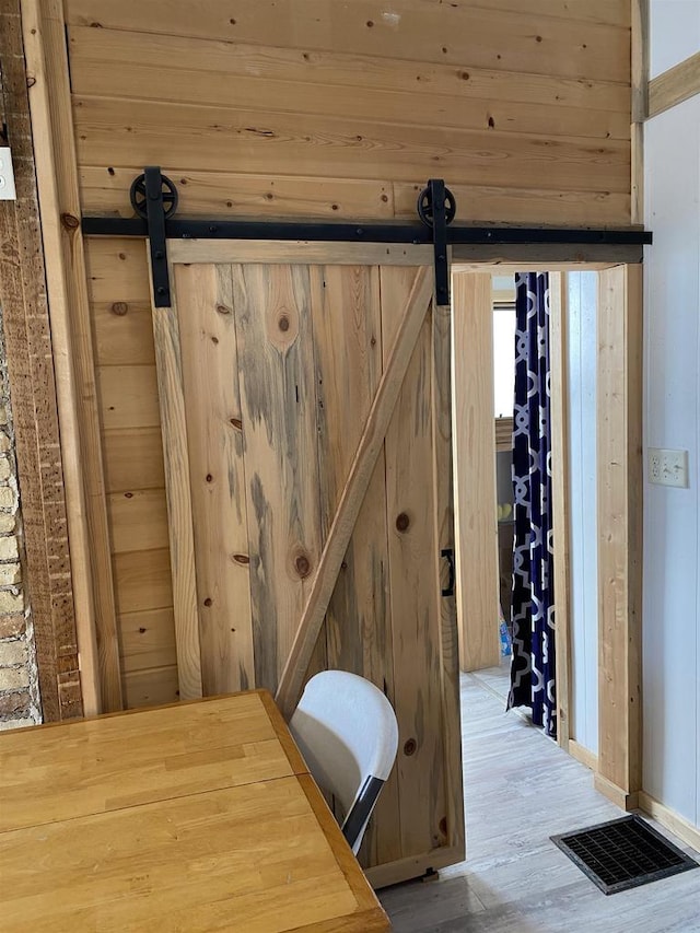 interior details with a barn door, wooden walls, visible vents, and wood finished floors