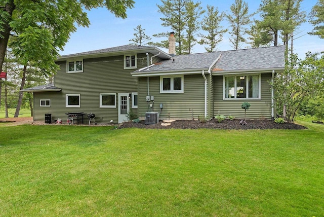 rear view of property with a shingled roof, a yard, a chimney, and central air condition unit