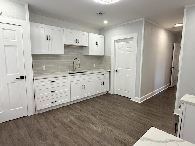 kitchen with decorative backsplash, dark wood-type flooring, white cabinets, a sink, and baseboards