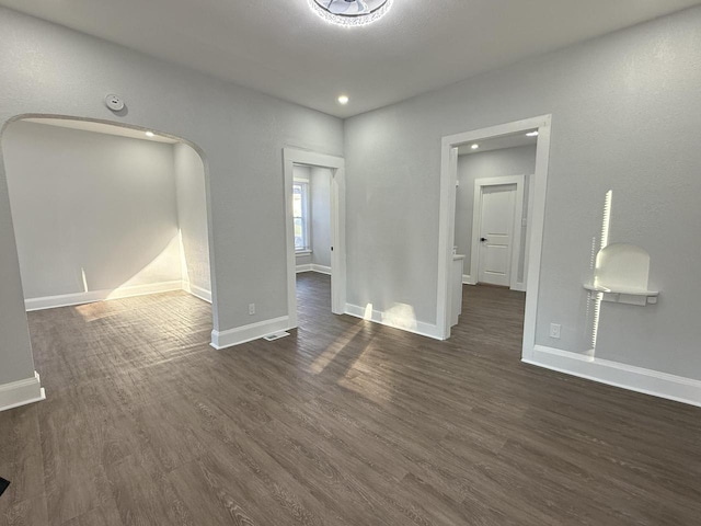 unfurnished room featuring arched walkways, recessed lighting, dark wood finished floors, and baseboards