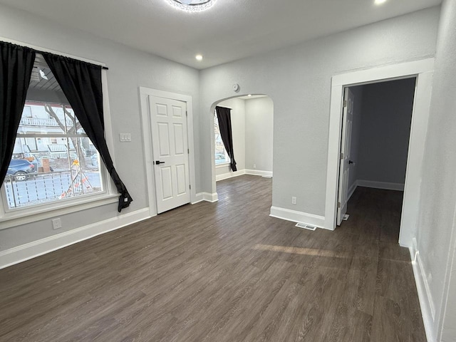 empty room with dark wood-style floors, arched walkways, recessed lighting, visible vents, and baseboards