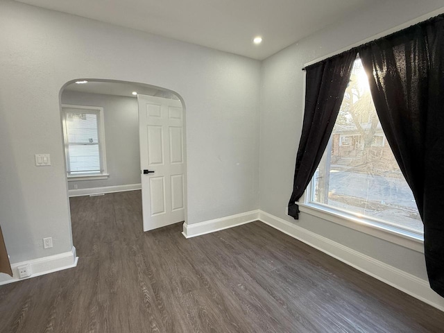 empty room featuring baseboards, arched walkways, dark wood finished floors, and recessed lighting