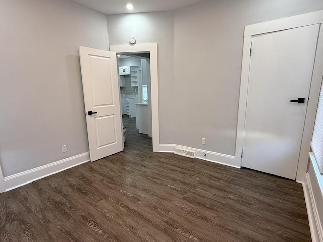 spare room with dark wood-type flooring, visible vents, and baseboards