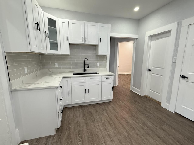 kitchen with dark wood-type flooring, a sink, white cabinets, backsplash, and glass insert cabinets