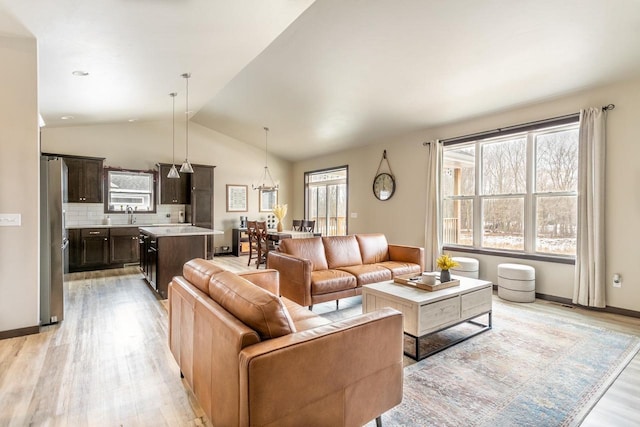 living room featuring light wood-type flooring, baseboards, vaulted ceiling, and a notable chandelier