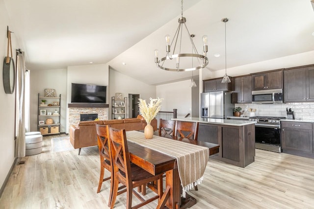 dining area with lofted ceiling, a fireplace, light wood-style flooring, and a notable chandelier