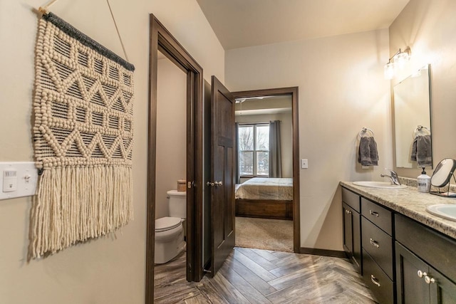 full bathroom featuring ensuite bathroom, toilet, a sink, baseboards, and double vanity