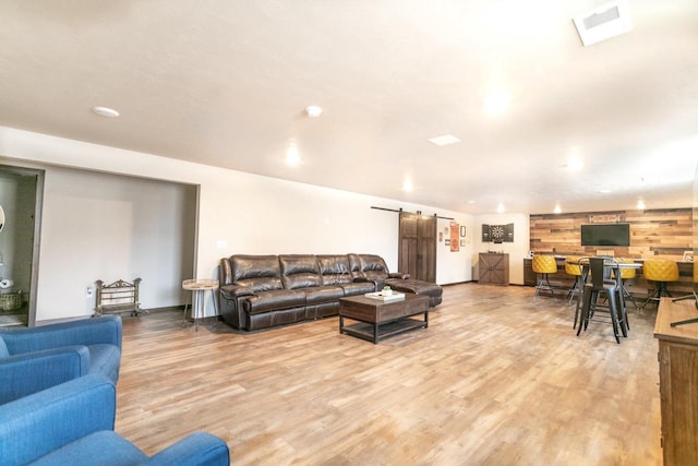 living area with visible vents, wood walls, light wood-style flooring, and a barn door