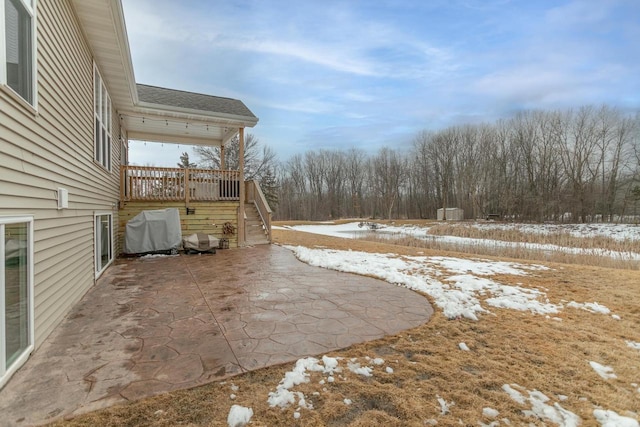 snowy yard with a wooden deck, stairway, and a patio