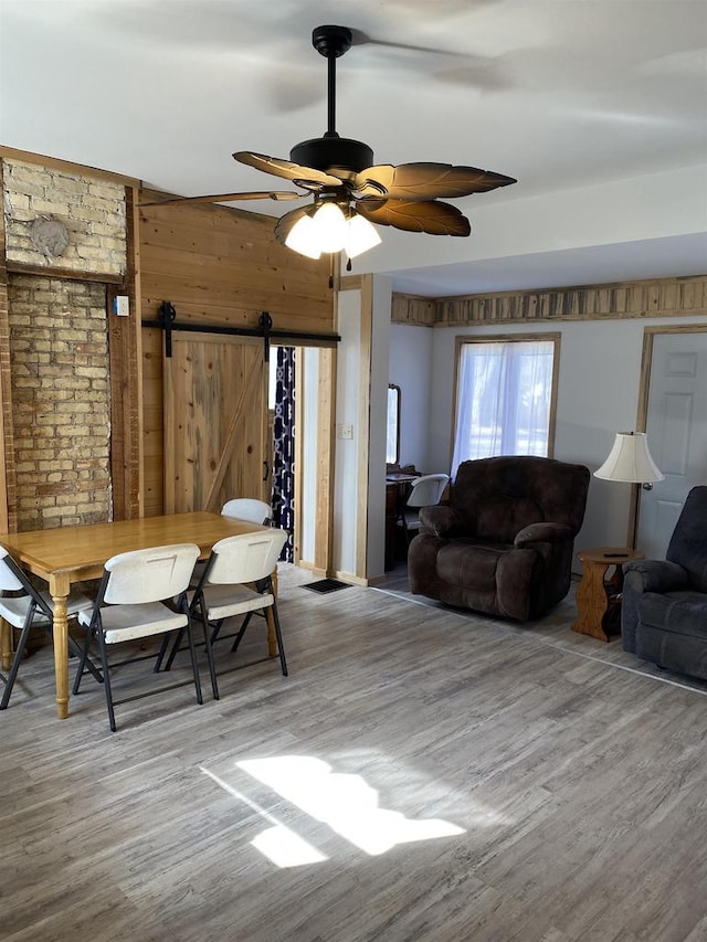 dining space featuring a barn door, ceiling fan, wooden walls, and wood finished floors