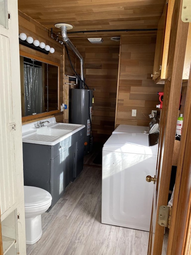 bathroom featuring water heater, toilet, wooden walls, wood finished floors, and washer and dryer