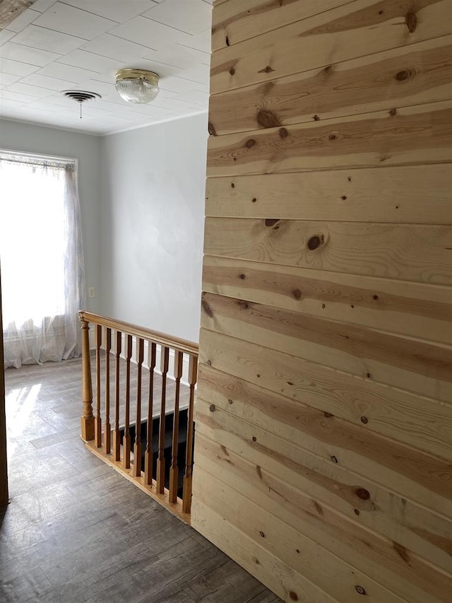 hallway featuring wood walls, visible vents, wood finished floors, and an upstairs landing