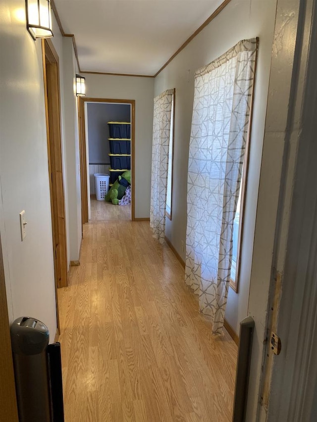 hall with light wood-style flooring, ornamental molding, and baseboards