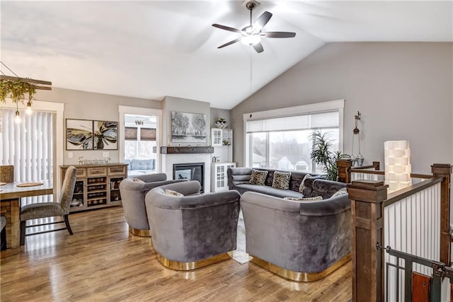 living room featuring vaulted ceiling, a glass covered fireplace, wood finished floors, and a healthy amount of sunlight