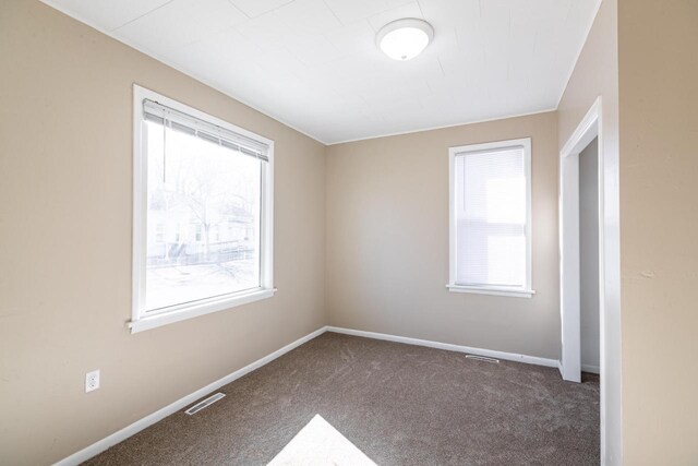 empty room with carpet floors, plenty of natural light, visible vents, and baseboards