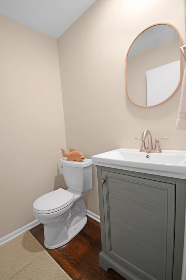 half bathroom featuring wood finished floors, vanity, toilet, and baseboards