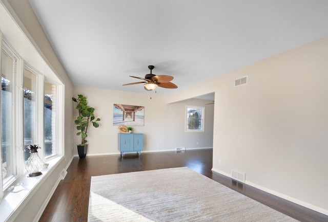 empty room with dark wood-style floors, baseboards, visible vents, and a ceiling fan