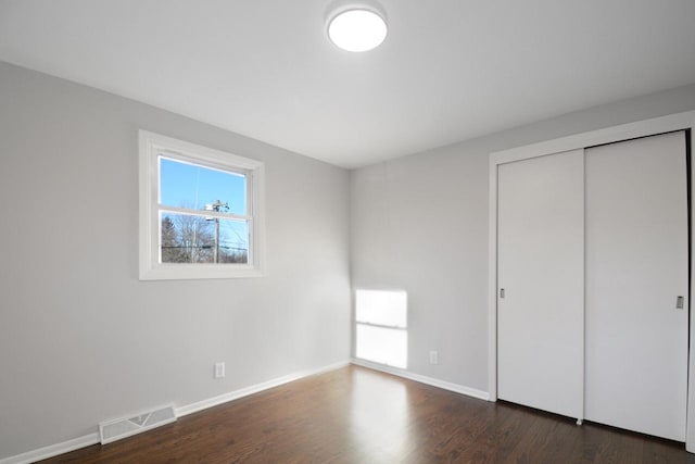 unfurnished bedroom with dark wood-style floors, baseboards, visible vents, and a closet