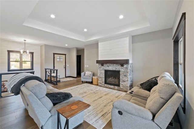 living room featuring a tray ceiling, a stone fireplace, recessed lighting, and wood finished floors