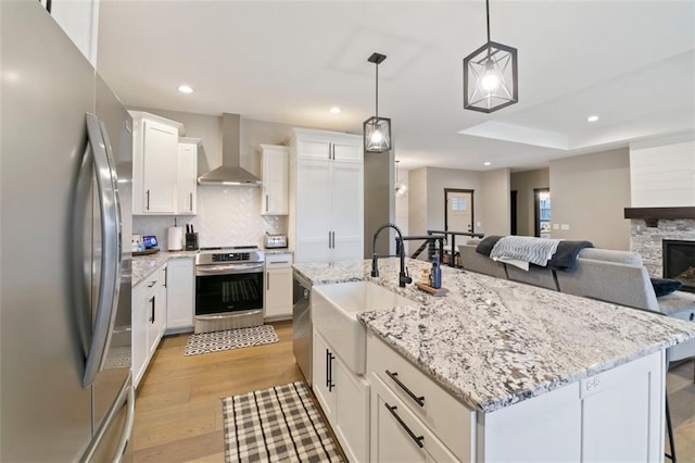 kitchen featuring stainless steel appliances, recessed lighting, light wood-style flooring, a sink, and wall chimney range hood