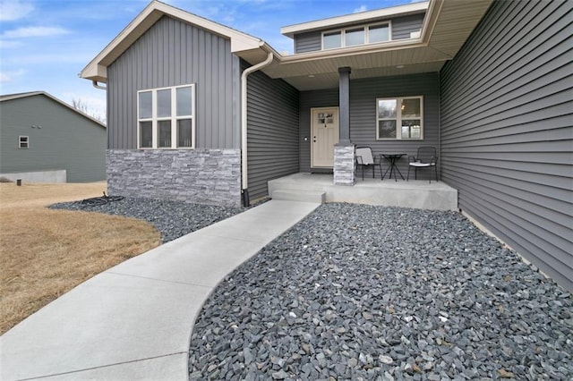 entrance to property featuring covered porch, stone siding, and board and batten siding