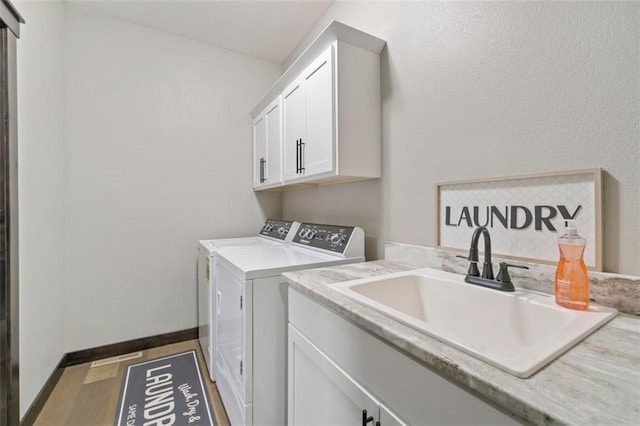 laundry area with cabinet space, baseboards, wood finished floors, washing machine and dryer, and a sink