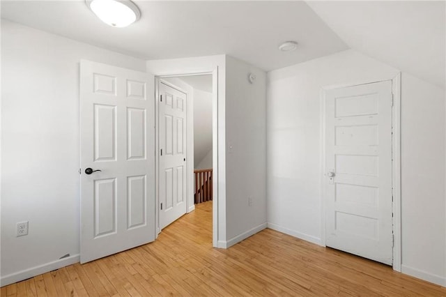 spare room featuring light wood-type flooring, lofted ceiling, and baseboards