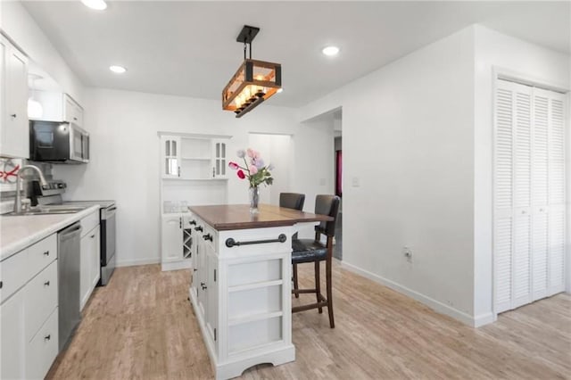 kitchen featuring open shelves, a sink, light wood-style flooring, and stainless steel appliances