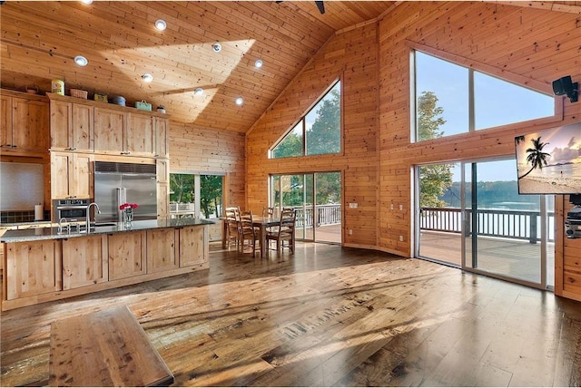 kitchen with wooden walls, wooden ceiling, wood-type flooring, a kitchen island with sink, and stainless steel built in refrigerator