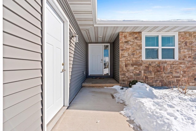 snow covered property entrance featuring stone siding