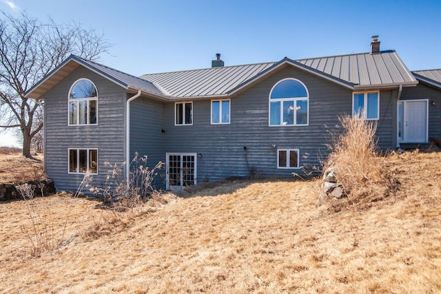 rear view of property with a chimney, a standing seam roof, and metal roof