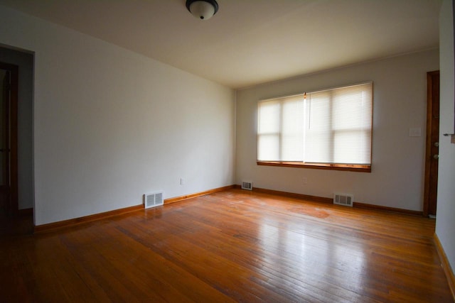 unfurnished room with wood-type flooring, visible vents, and baseboards